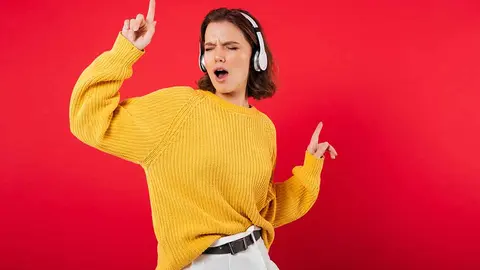 Portrait of a cheerful woman in headphones listening to music and dancing isolated over pink background
